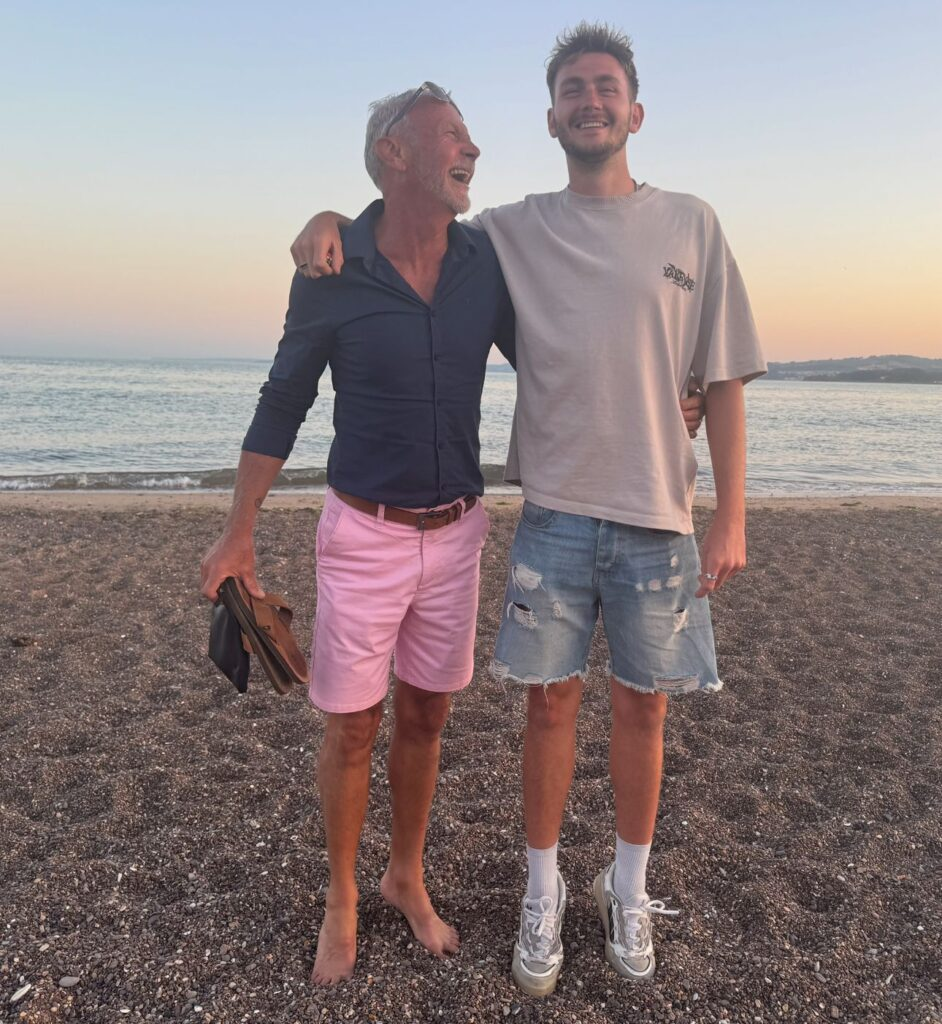 Father and son on a beach at sunset, arm in arm, laughing together