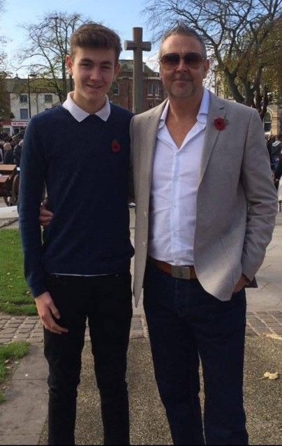 Tyrone and his son standing together outdoors, both wearing poppy pins on their lapels