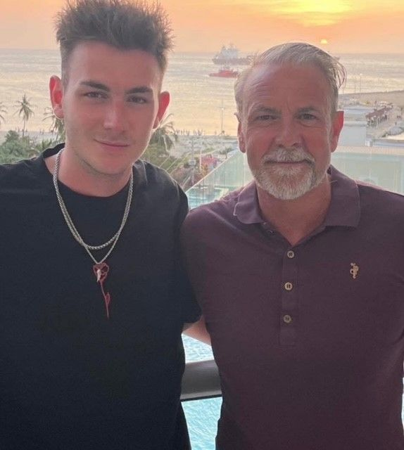 Tyrone and his son together on a balcony at sunset with the sea behind them